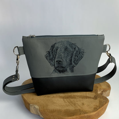 Umhängetasche mit Flat Coated Retriever-Motiv aus Kunstleder, zweifarbig, oben dunkelgrau, unten schwarz. Stickmotiv oben: Flat coated Retriever-Kopf mit Blick zur Seite, gestickt in schwarz.