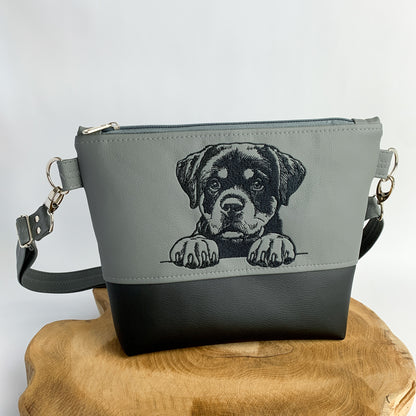 Umhängetasche mit Rottweiler-Motiv, der kleine Rottweiler schaut über seine Pfoten hinweg. Die Tasche ist handgefertigt, bestickt und aus Kunstleder genäht. zweifarbig, oben dunkelgrau mit Motiv in schwarz, unten schwarz