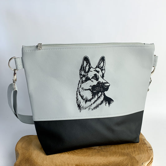 handgefertigte Umhängetasche mit Schäferhund-Motiv bestickt, aus Kunstleder, zweifarbig unterteilt, oben hellgrau, unten schwarz, Motiv schwarz auf hellgrau gestickt als detailreiche Silhouette.