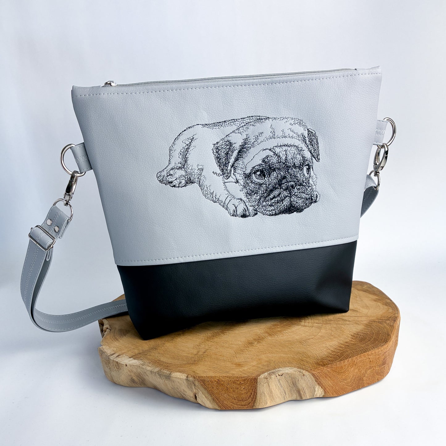 Umhängetasche/Handtasche aus Kunstleder mit Mops-Motiv bestickt, zweifarbig, oben hellgrau, unten schwarz. der Mops ist in schwarzer Kontur detailreich gestickt. liegt auf den Vorderpfoten